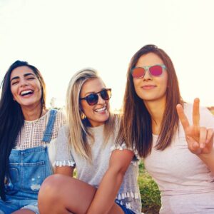 Tre giovani adulte sorridono all'aperto. Immagine utilizzata per presentare il gruppo "Keep Calm and Love Young Adults" di GenitoriChe OdV dedicato ai genitori con figli giovani adulti.